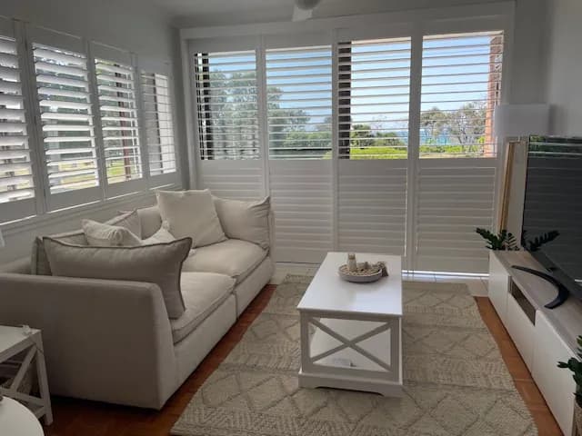 White plantation shutters across a beachside lounge room — one of our own jobs