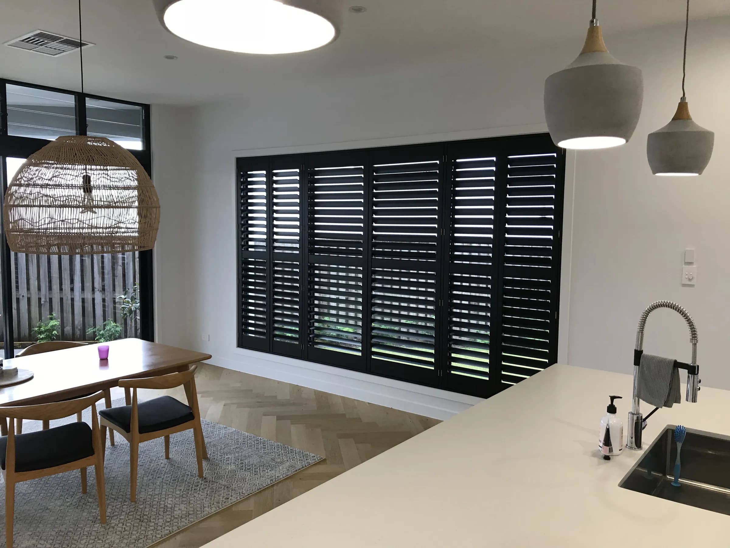 Black plantation shutters across a wide window in an open-plan kitchen and dining room — one of our own jobs