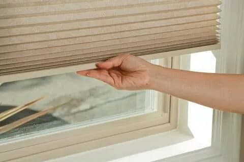 A cordless honeycomb blind being raised by hand from its bottom rail
