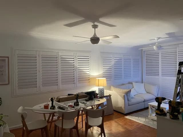 Newly fitted white plantation shutters in a lounge room, the installer's tools still on the table — one of our own jobs