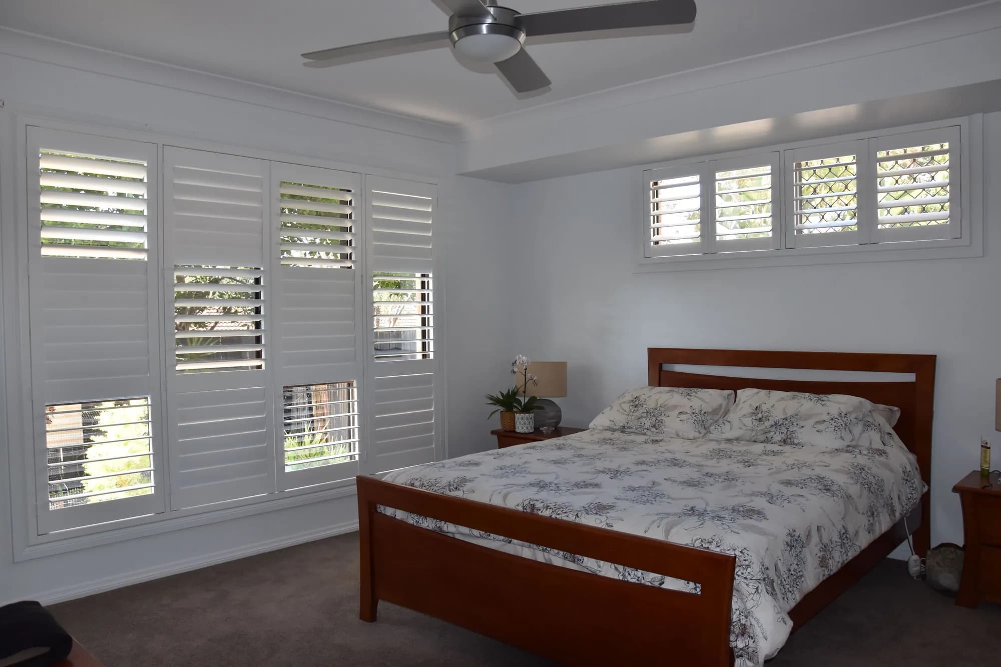 Matching white plantation shutters on every window of a bedroom, highlight windows included — one of our own jobs
